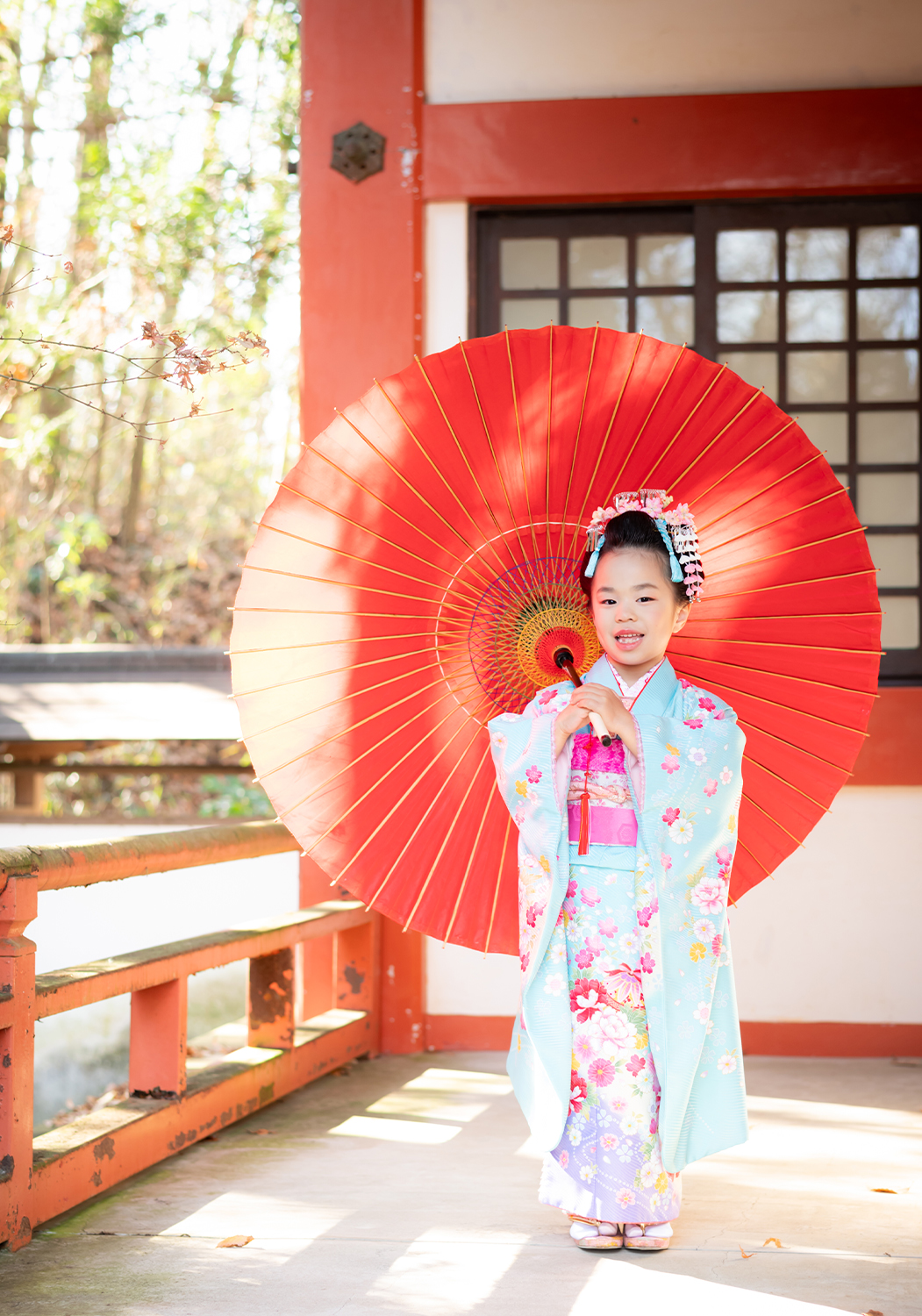 神社の境内で赤い番傘を持っている七五三7歳女の子